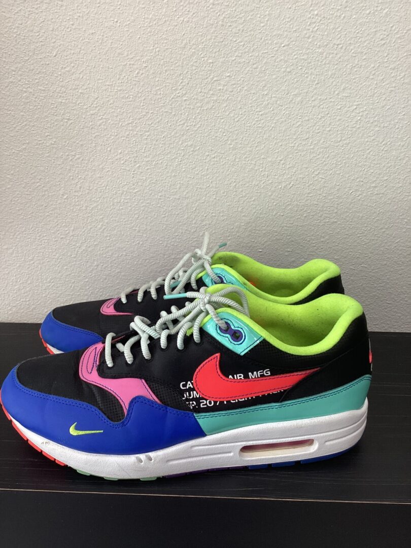 A pair of colorful Pre-Owned Air Max sneakers with a mix of blue, pink, green, and black colors, displayed on a white surface against a black background.