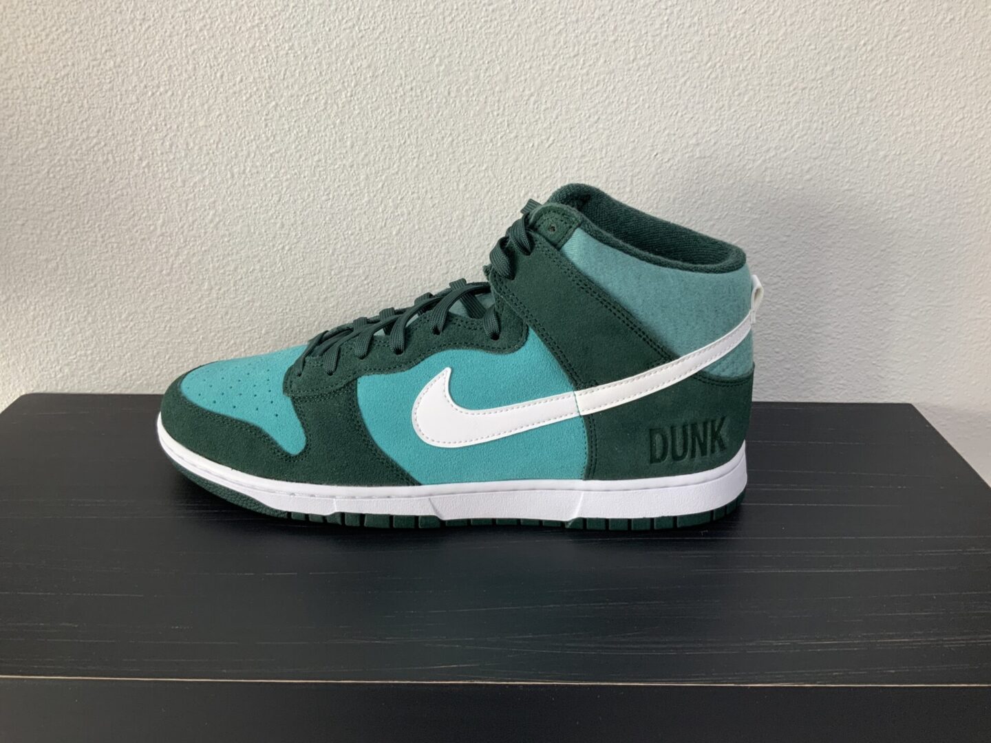 A single teal and white High top Dunk SE (Athletic Club - Pro Green) sneaker displayed on a black shelf against a neutral background.