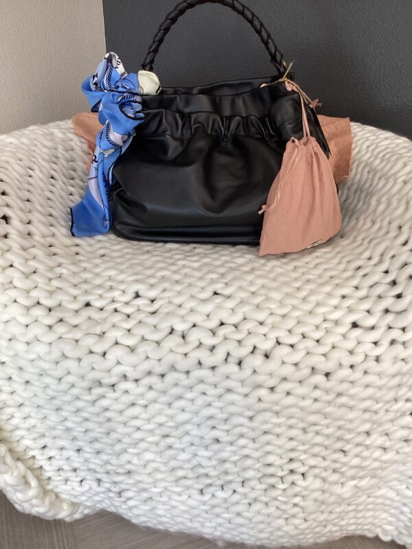 A Burberry Bucket Bag with a blue figurine keychain and a peach scarf, placed on a textured white knitted blanket.