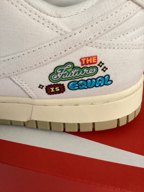 Close-up of a Nike Dunk Low sneaker with the phrase "the future is equal" embroidered in colorful letters on the side, set against a red background.