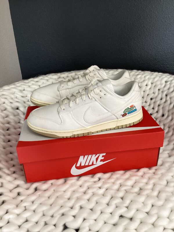 A pair of white Nike Dunk Low sneakers on a red Nike Dunk Low shoebox, placed on a white textured surface.