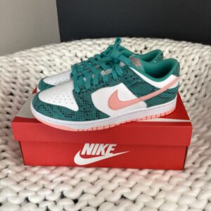 A pair of turquoise and white Nike-Dunk Low ME Teal/Bleached Coral sneakers displayed on a red Nike-Dunk Low ME Teal/Bleached Coral box, which is placed on a white textured surface.