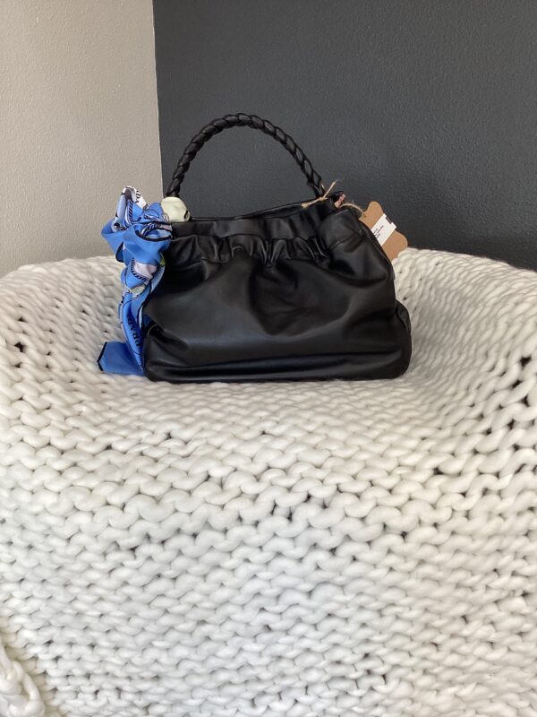 A black Burberry Bucket Bag with braided handles and a blue scarf tied to it, resting on a textured, white knit chair.