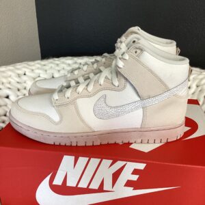A white Nike Dunk Hi Retro high-top sneaker displayed on a red Nike Dunk Hi Retro shoebox against a gray background.