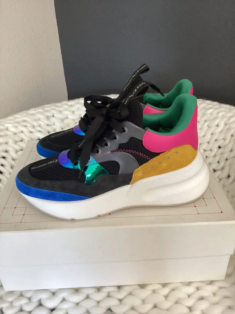 A pair of colorful sneakers with black laces, featuring a combination of pink, green, yellow, and blue suede patches, resting on a white box.