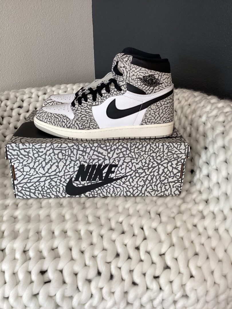 A pair of Air Jordan 2 Retro sneakers with a white and black crackled design, displayed on a white textured rug above its matching shoe box.