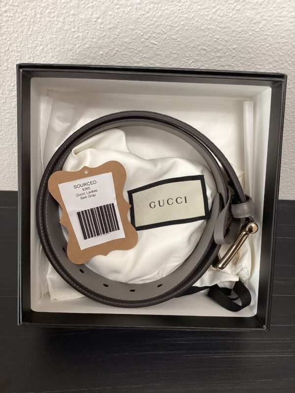 A gucci belt with a gold buckle, packaged in its original box with a white satin lining and brand tags attached.