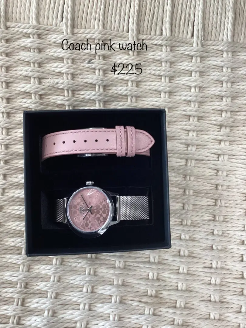 A pink coach watch displayed in an open black box, resting on a woven mat, with a price tag of $225 displayed at the top.