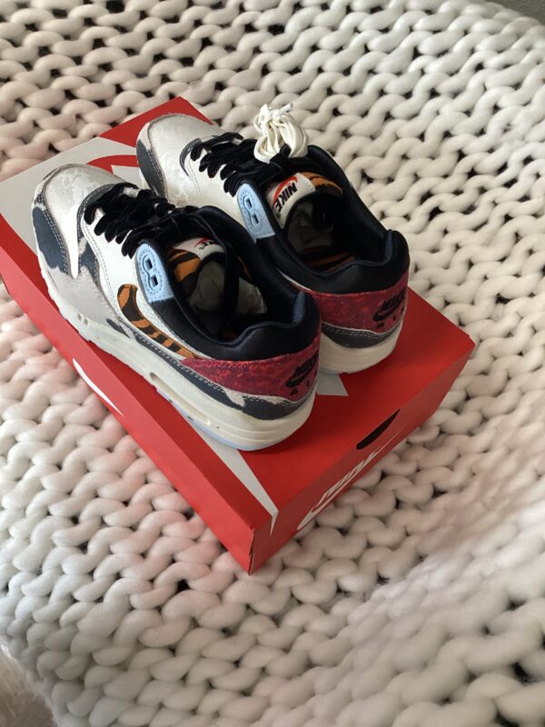 A pair of Air Jordan 2 Retro sneakers with black, white, and orange colors, placed on their shoebox on top of a white knitted blanket.