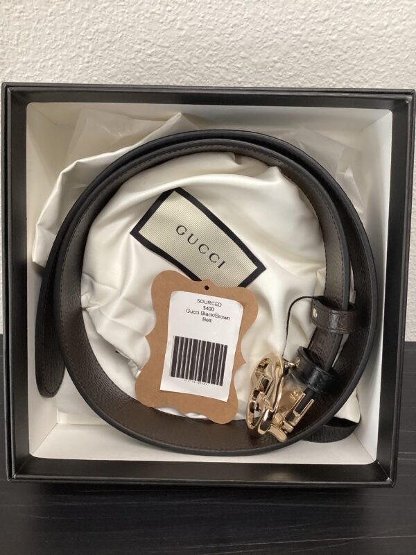 A gucci leather belt with a gold buckle, displayed in its original packaging with labels.