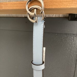 A light blue leather belt with a silver buckle hangs from a wooden rod.