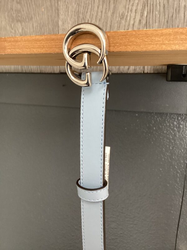 A light blue leather belt with a silver buckle hangs from a wooden rod.