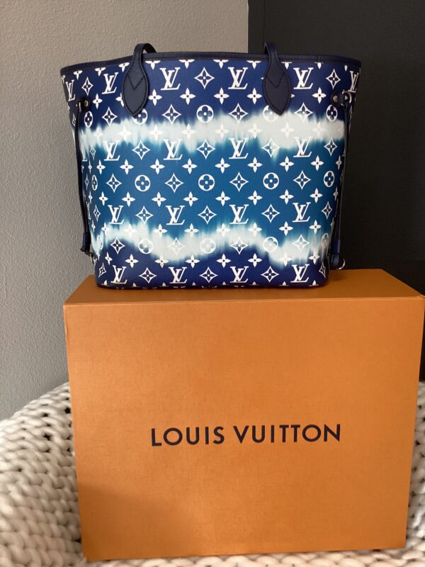 LV MM Neverfull Bag with blue and white monogram pattern, resting on top of an orange louis vuitton box against a gray background.