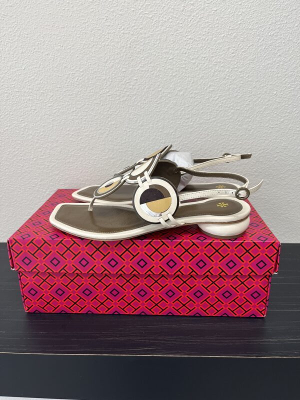 A pair of Tory Burch Disk Sandals placed on a red and pink patterned shoe box on a gray surface.