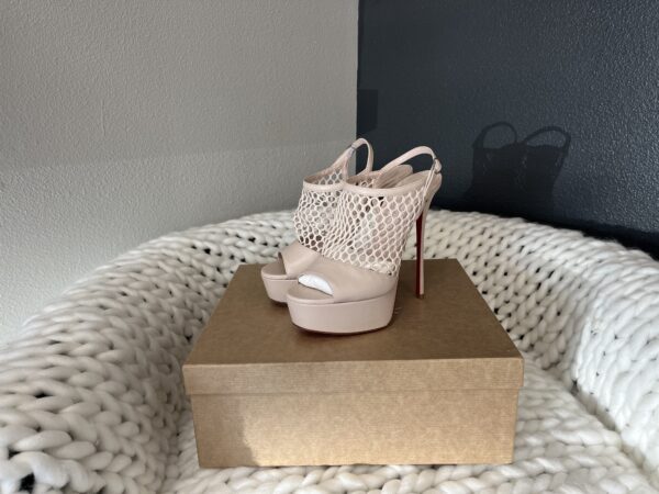 A pair of Christian Louboutin high-heeled shoes on a cardboard box, placed on a white knitted blanket against a gray wall.