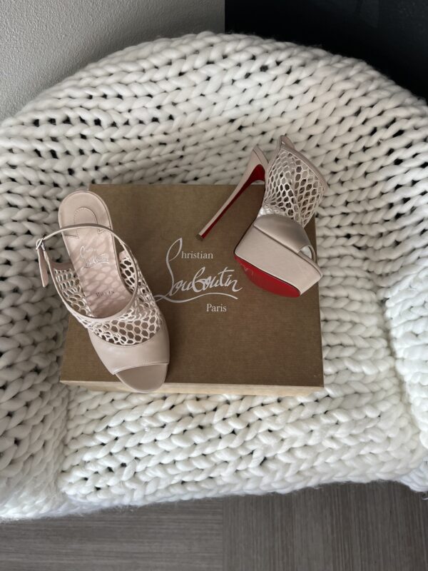 A pair of Christian Louboutin high heels with signature red soles on a box, placed next to a white knitted throw.