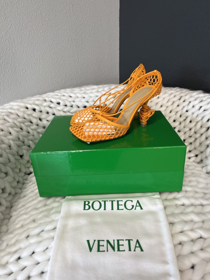 Orange high-heeled shoe on a green Bottega Veneta box with a white dust bag.