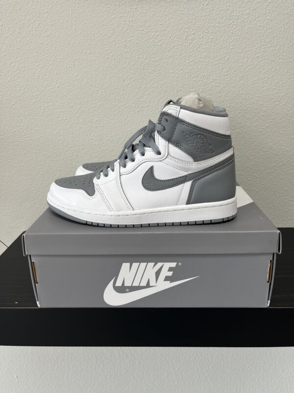 A pair of grey and white Jordan 1 High Stealth-Grey White sneakers displayed on top of a nike shoe box on a table.