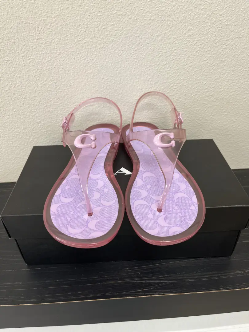 A pair of pink Coach Jelly with circular patterns on the insole, displayed on a black box on a beige surface.