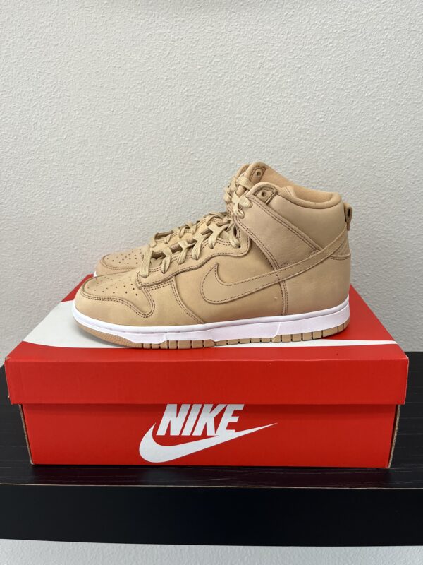 A pair of beige Nike Dunk High Brown high-top sneakers displayed on a red Nike Dunk High Brown shoebox against a neutral background.