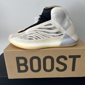 A modern sporty sneaker displayed on an Adidas YZY QNTM labeled box, featuring a white and gray zebra stripe design and a beige sole.