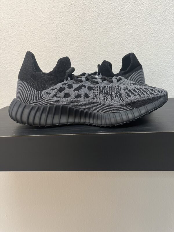 A pair of Adidas YEZY 350 V2 CMPCT sneakers with thick textured soles, displayed on a black shelf against a white wall.