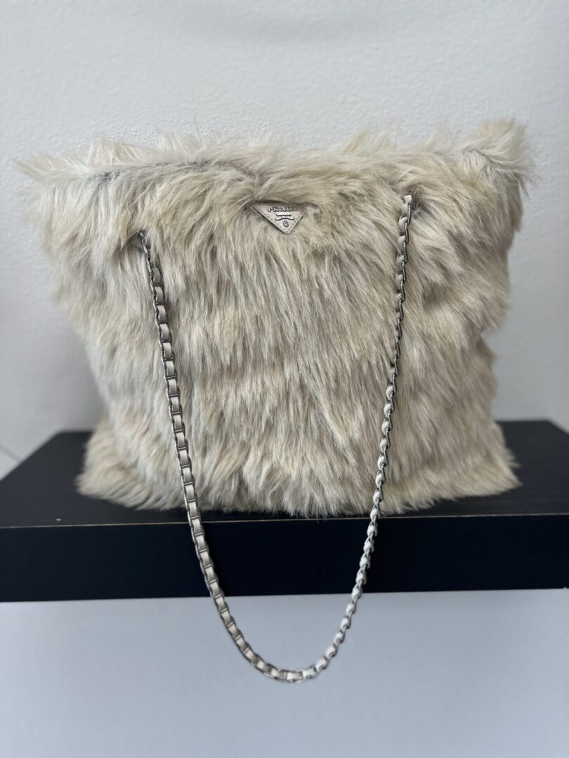 Chain Fur Bag with a silver chain strap sitting on a black box against a white background.