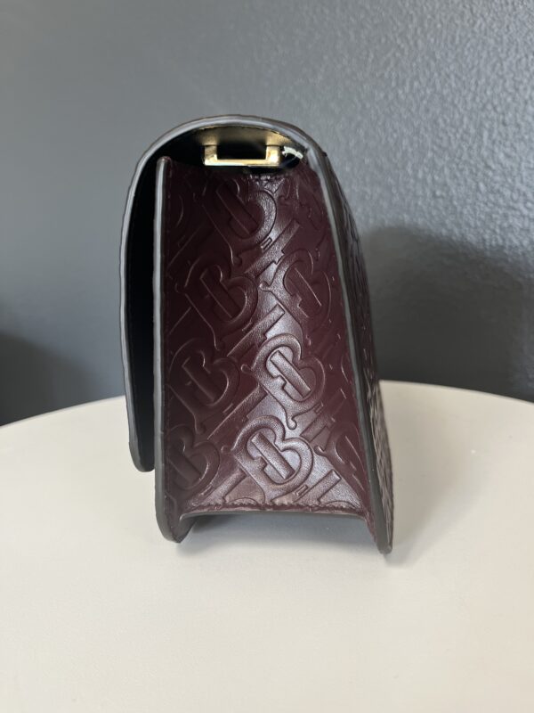 A Gucci Black Handbag with embossed patterns, standing upright on a white surface against a grey background.