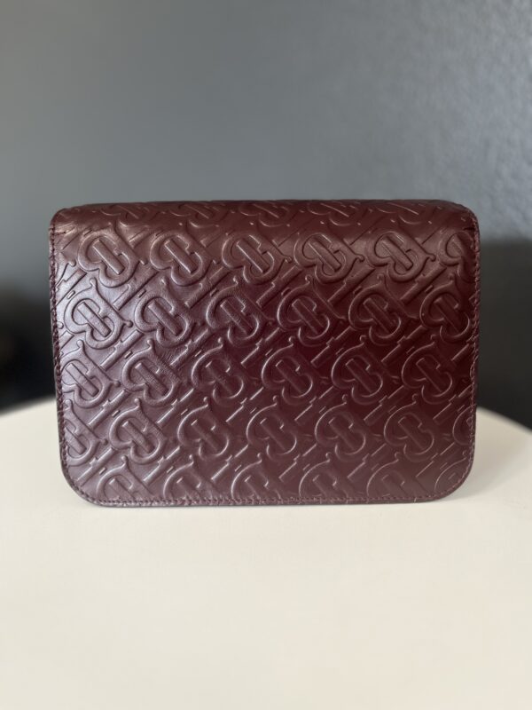 A Gucci black handbag with an embossed geometric pattern, resting on a white surface against a gray background.